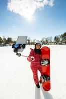 donna con lo snowboard che usa lo smartphone su un bastone per fare selfie foto