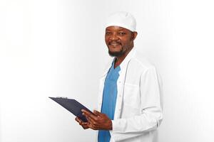 sorridente nero chirurgo medico barbuto uomo nel bianca cappotto e berretto con medico record su appunti foto