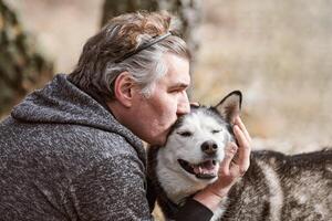 adulto uomo nel grigio felpa abbracci e baci siberiano rauco cane, vero amore di umano e animale domestico foto