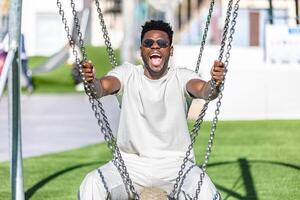 sorridente afroamericano uomo seduta su un' swing nel un' parco. foto