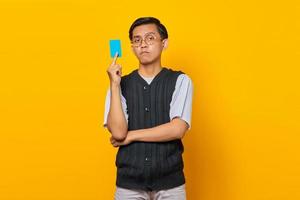 ritratto di giovane uomo asiatico scioccato che mostra la carta di credito su sfondo giallo foto