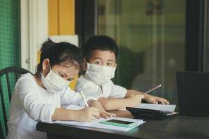 studente asiatico che indossa una maschera protettiva che impara da computer e smartphone foto