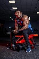 muscolare afro americano gli sport uomo guardare a telecamera al di sopra di nero Palestra sfondo. Perfetto muscolare corpo con forte muscoli. foto