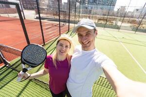 giovane coppia di tennis Giocatori indossare un' abbigliamento sportivo Tenere un' racchetta su loro le spalle e un' palla nel un' mano in piedi all'aperto su tennis Tribunale a presto mattina foto