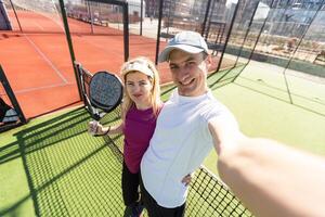 giovane coppia di tennis Giocatori indossare un' abbigliamento sportivo Tenere un' racchetta su loro le spalle e un' palla nel un' mano in piedi all'aperto su tennis Tribunale a presto mattina foto