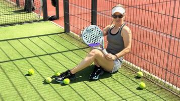 ritratto di attivo emotivo donna giocando padel tennis su Aperto Tribunale nel estate, oscillante racchetta per ritorno palla al di sopra di netto .. foto