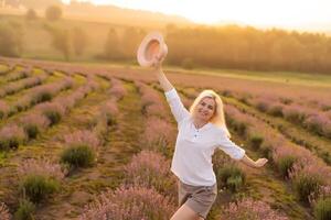 giovane biondo donna viaggiatore indossare cannuccia cappello nel lavanda campo circondato con lavanda fiori. foto