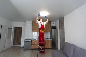 giovane uomo installazione soffitto lampada su scaletta nel cucina foto