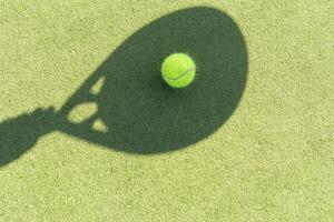 ombra di un' padel racchetta con un' giallo palla su il verde erba. foto