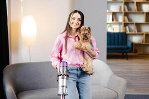 donna con vuoto addetto alle pulizie e cane nel sua mano passare l'aspirapolvere nel il vivente camera. foto