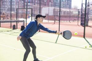 un' ragazza nel abbigliamento sportivo è formazione su un' pagaia tennis Tribunale. il ragazza è colpire il palla contro il bicchiere per rendere un' rimbalzo. concetto di donne giocando pagaia. foto