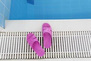 rosa pantofole In piedi di il piscina con blu acqua su un' luminosa, soleggiato giorno. foto