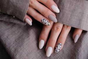 donna di mano con un' bellissimo di forma ovale manicure. autunno tendenza, beige colore lucidatura con leopardo modello su Chiodi con gel polacco, Gommalacca. foto