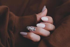 donna di mano con un' bellissimo di forma ovale manicure. autunno tendenza, beige colore lucidatura con leopardo modello su Chiodi con gel polacco, Gommalacca. foto