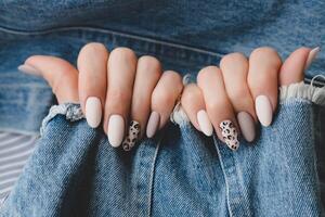 donna di mano con un' bellissimo di forma ovale manicure. autunno tendenza, beige colore lucidatura con leopardo modello su Chiodi con gel polacco, Gommalacca. foto