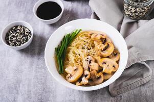 asiatico la minestra con riso tagliatelle, funghi e verde cipolle nel un' ciotola su il tavolo foto