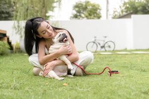 contento asiatico donna giocando con carino inteligente carlino cucciolo cane nel il Giardino dietro la casa foto