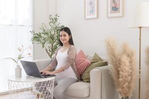 incinta donna Lavorando su il computer portatile e inteligente Telefono nel il vivente camera a casa foto