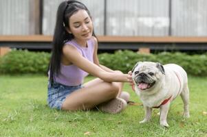 contento asiatico donna giocando con carino inteligente carlino cucciolo cane nel il Giardino dietro la casa foto