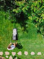 caucasico giardiniere falciatura Giardino dietro la casa giardino erba utilizzando cordless elettrico erba tosaerba. aereo Visualizza. foto