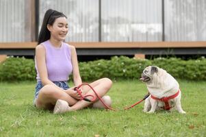 contento asiatico donna giocando con carino inteligente carlino cucciolo cane nel il Giardino dietro la casa foto