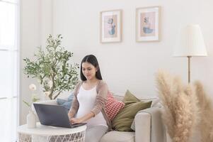 incinta donna Lavorando su il computer portatile e inteligente Telefono nel il vivente camera a casa foto