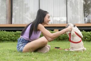 contento asiatico donna giocando con carino inteligente carlino cucciolo cane nel il Giardino dietro la casa foto