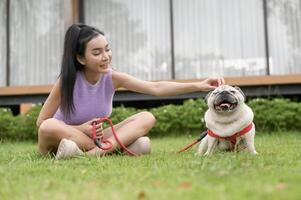 contento asiatico donna giocando con carino inteligente carlino cucciolo cane nel il Giardino dietro la casa foto