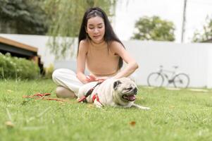 contento asiatico donna giocando con carino inteligente carlino cucciolo cane nel il Giardino dietro la casa foto