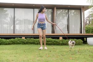 contento asiatico donna giocando con carino inteligente carlino cucciolo cane nel il Giardino dietro la casa foto