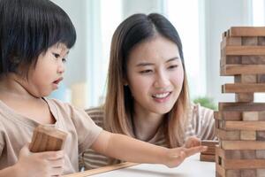 Asia contento singolo madre giocando apprendimento Giochi janga con il poco ragazza. divertente famiglia è contento e eccitato nel il Casa. là e figlio avendo divertimento la spesa tempo insieme. vacanza, fine settimana, vacante. foto