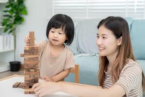 Asia contento singolo madre giocando apprendimento Giochi janga con il poco ragazza. divertente famiglia è contento e eccitato nel il Casa. là e figlio avendo divertimento la spesa tempo insieme. vacanza, fine settimana, vacante. foto