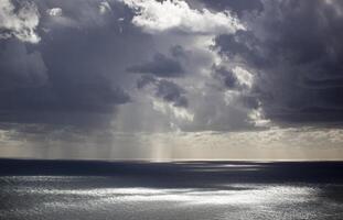 nuvoloso grigio cielo con Basso strutturato nuvole. luce del sole sbircia attraverso il nuvole e cascate su il mare. sfondo. orizzontale foto