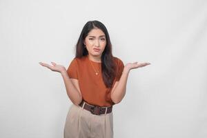 bellissimo giovane asiatico donna indossare un' Marrone camicia sembra così confuso, isolato di un' bianca sfondo. foto