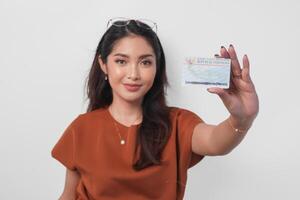 fiducioso giovane asiatico donna indossare Marrone camicia è mostrando identità carta Indonesia per il telecamera al di sopra di bianca sfondo. foto