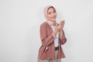 religioso giovane asiatico musulmano donna nel hijab fare preghiere gesto mentre sorridente per il telecamera isolato bianca sfondo. foto