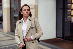 ritratto di elegante donna nel cappotto in piedi su città strada sfondo e guardare a lato foto