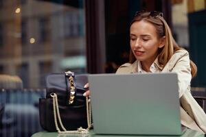 attraente europeo donna Lavorando su il computer portatile in linea mentre seduta a all'aperto bar terrazza foto