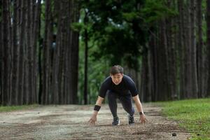 asiatico pista corridore è in esecuzione all'aperto nel pino foresta sporco strada per esercizio e allenarsi attività formazione mentre concentrato su il inizio posizione per gara per salutare stile di vita e fitness concetto foto