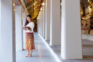 asiatico buddista donna è lettura sanscrito antico tripitaka libro di signore Budda dhamma insegnamento mentre visitare il tempio per cantilenando e culto dentro il monastero foto