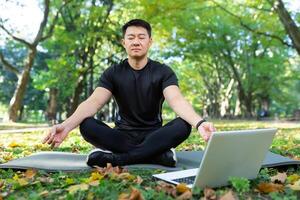 asiatico Meditare esercizio nel loto posa, uomo riposo dopo fitness formazione utilizzando il computer portatile per in linea meditazione addestramento. foto