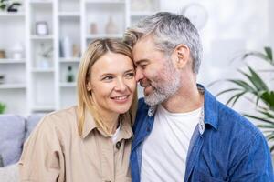 romantico contento mezzo età coppia rilassante su divano a casa, sorridente, amorevole maturo coppia rilassante nel accogliente vivente camera interno, coccole su divano, godendo fine settimana insieme, copia spazio. foto