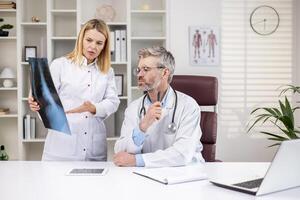 grave maturo medici pensiero e discutere del paziente raggi X, uomo e donna nel medico bianca cappotti Lavorando dentro clinica ufficio, Lavorando consultare. foto