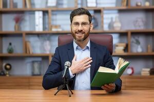 un' uomo, un' pastore di un' Chiesa, un' religioso Comunità di vario denominazioni, conduce il suo sermone in linea. seduta e A proposito di nel davanti di il telecamera con un' santo prenotare, Tenere il suo mano su il suo cuore. foto