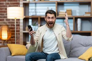 contento giovane uomo Tenere Telefono nel mano, contento e festeggiare, guardare e urlando a telecamera. avuto bene notizia, messaggi, ha vinto il lotteria, scommessa su il gioco. foto