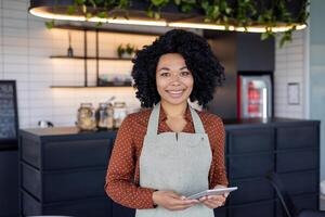 ritratto cameriera di un' piccolo attività commerciale proprietario di un' bar, donna nel grembiule sorrisi e sembra a telecamera con un' tavoletta computer nel sua mani, un dipendente di un' bar di un' ristorante vicino un' caffè contatore. foto