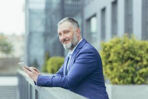 ritratto di riuscito anziano dai capelli grigi uomo d'affari capo, uomo al di fuori ufficio utilizzando tavoletta computer sorridente e guardare a telecamera, investitore nel attività commerciale completo da uomo, contento banchiere foto