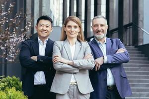 femmina attività commerciale capo e sua diverso squadra, asiatico uomo guardare a telecamera con attraversato braccia e sorridente, sognare squadra al di fuori ufficio edificio foto