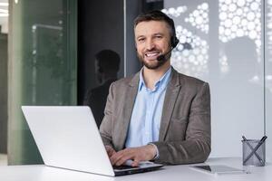 sorridente uomo d'affari con cuffia Lavorando su il computer portatile nel moderno ufficio ambientazione, incarnando professionalità e cliente servizio. foto