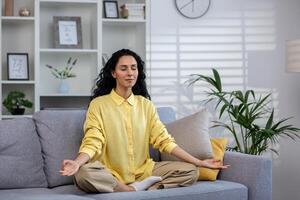 giovane bellissimo ispanico donna solo a casa Meditare seduta su divano nel loto posizione, donna con Riccio capelli nel vivente camera con Riccio capelli con chiuso occhi riposo rilassante. foto